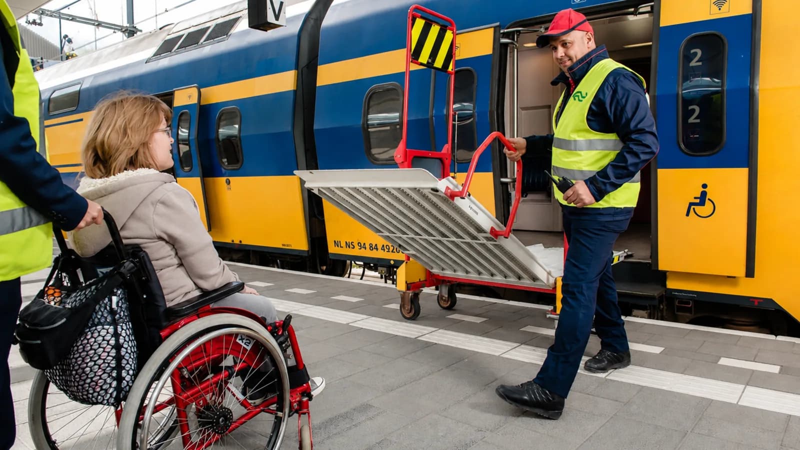Medewerker met veiligheidshesje rijdt een rolstoeloprijplaat naar de deur van een trein