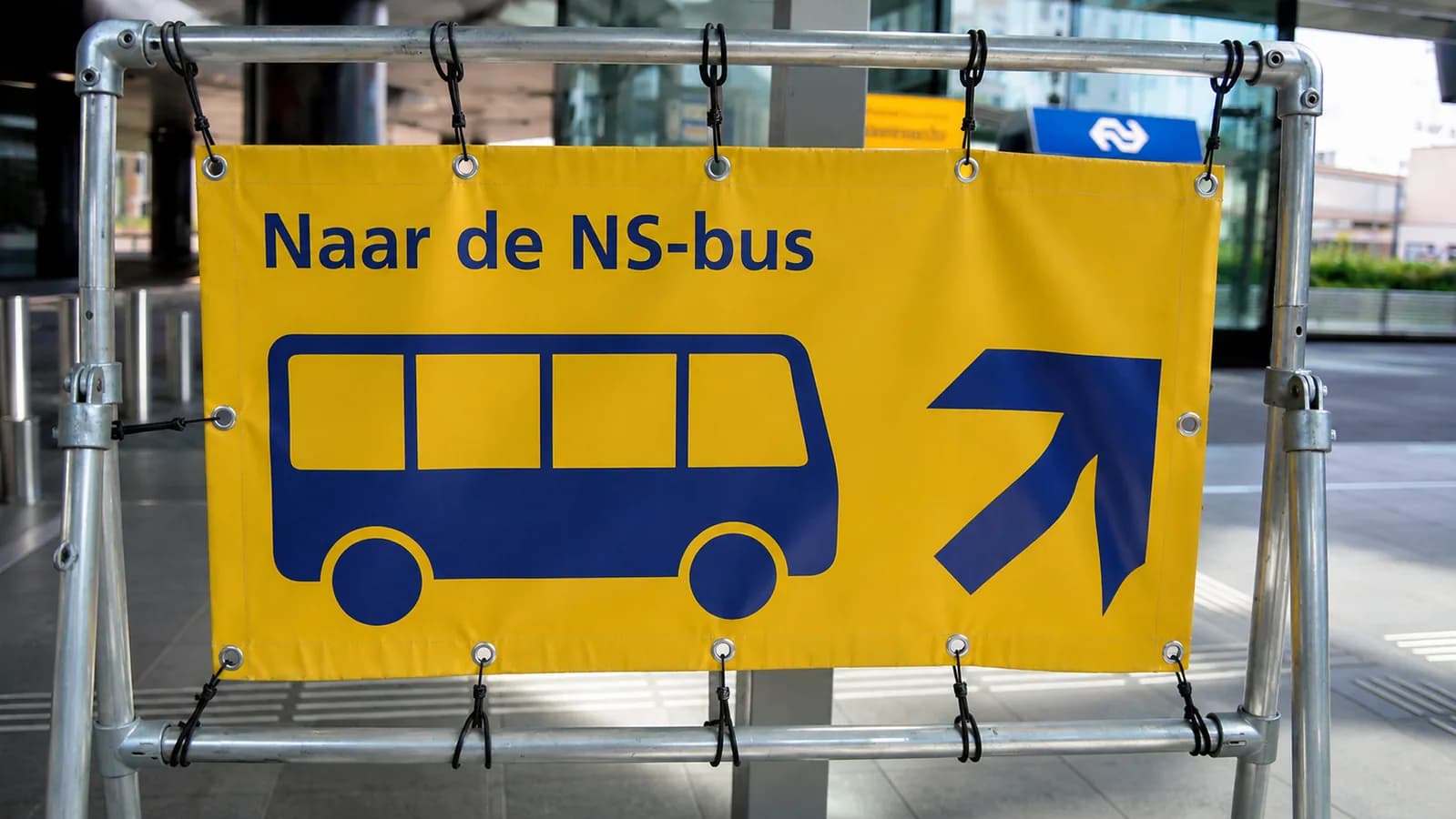 Geel bord op een stationsplein dat reizigers naar de vervangende NS-bus wijst